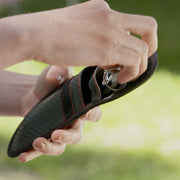 Person holding a black Key Guard pouch with red stitching against a blurred green background