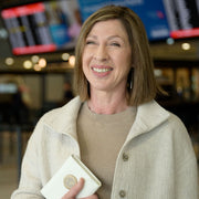 Woman smiling at an airport holding a white passport wallet.
