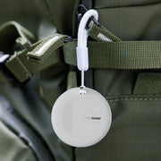 White round Travel Traka with a carabiner attached to a green backpack